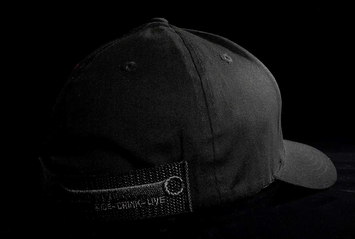 A Fourfive 45 Knight Racer hat with curved brim in all black stretch fit material with its 45 degree back right view showing the hat holster mount and its embroidery detail in dramatic lighting with black background.   Built to fit normal and big heads.