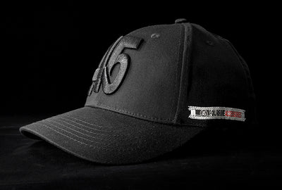 A Fourfive 45 Knight Racer hat with Curved brim in all black stretch fit material and a 45 logo embroidery detail in the front with the hat facing 45 degrees to the left in dramatic lighting with black background.  Built to fit normal and big heads.