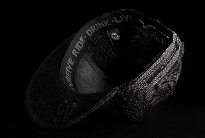A Fourfive 45 Customizer hat shadow edition with flat brim black cotton front and black velcro logo detail for customising and black mesh back  flipped over showing the 45 logo embroidery detail on the bottom of the brim and the ride drink live embroidery detail around the sweat band on the inside of the hat.  Built to fit normal and big heads.