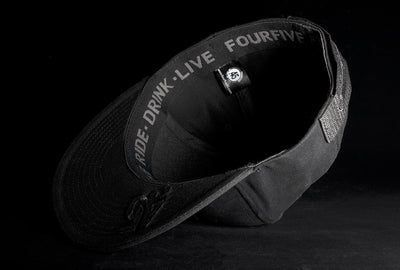 A Fourfive 45 Revolver hat black edition with flat brim in all black stretch fit material flipped over showing the 45 logo embroidery detail on the bottom of the brim and the ride drink live embroidery detail around the sweat band on the inside of the hat.  Built to fit normal and big heads.