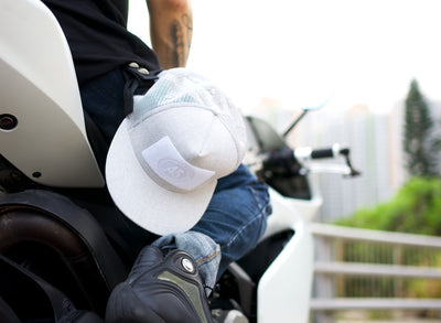 A Fourfive 45 Customizer hat snow edition with flat brim light grey cotton front and white velcro logo detail for customising and light grey mesh back holstered on to a riders hat holster while he sits on a white ducati panagale. Built to fit normal and big heads.