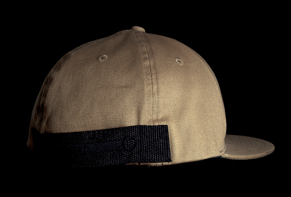 A Fourfive 45 Revolver hat sand edition with flat brim in a khaki coloured stretch fit material with its 45 degree back right view showing the hat holster mount and its embroidery detail in dramatic lighting with black background.  Built to fit normal and big heads.