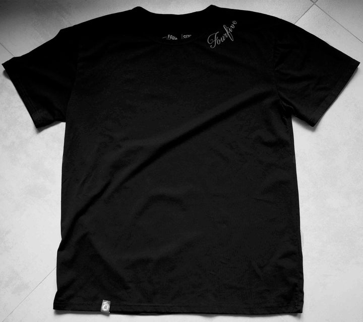 A Fourfive 45 black tattoo t shirt with the Fourfive tattoo graphics on the left side of the collar sitting on a concrete back ground.