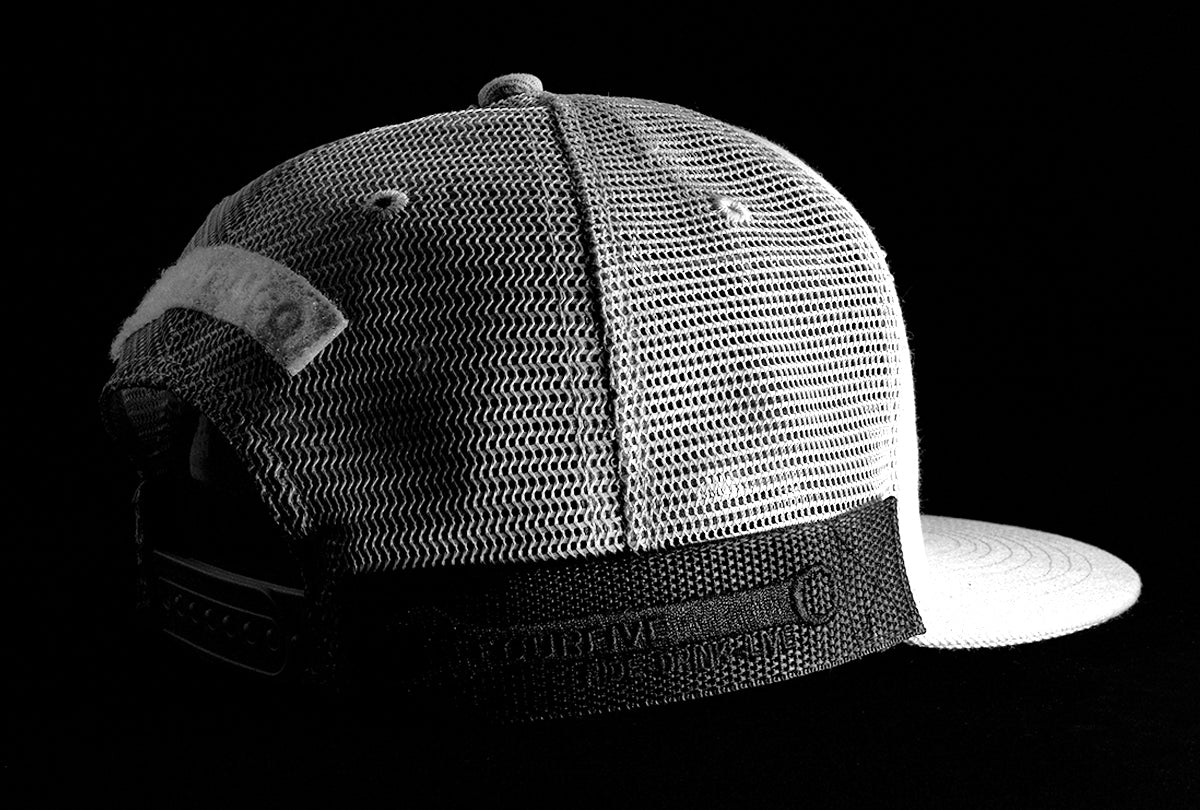 A Fourfive 45 Customizer hat snow edition with flat brim light grey cotton front and white velcro logo detail for cuctomising and light grey mesh back with snapback with its 45 degree back view showing the velcro detail and the hat holster mount with its embroidery details in dramatic lighting with black background.  Built to fit normal and big heads.