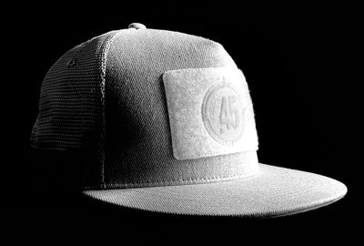 A fourfice 45 Customizer hat snow edition with flat brim light grey cotton front with white velcro logo detail for customising and light grey mesh back with snapback facing 45 degrees right in dramatic lighting with black background.  Built to fit normal and big heads.