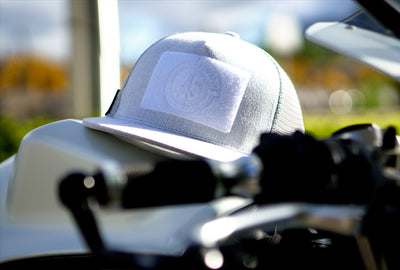 A Fourfive 45 Customizer hat snow edition with flat brim light grey cotton front with white velcro logo detail for customising with your own velcro patches and light grey mesh back with snapback sitting on a white Ducati Panagale in summer afternoon light.  Built to fit normal and big heads.