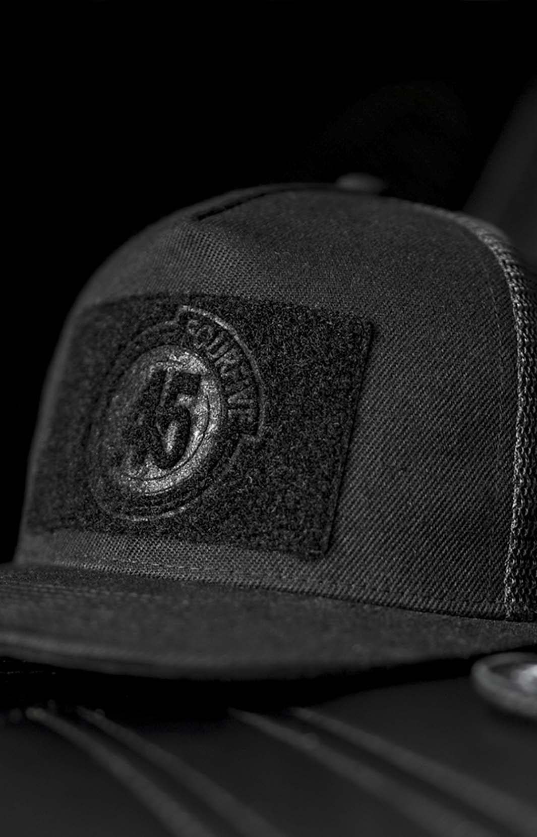Fourfive 45, all black flat brim snap back customizer hat with velcro elements on front and back sitting on a black leather armchair.