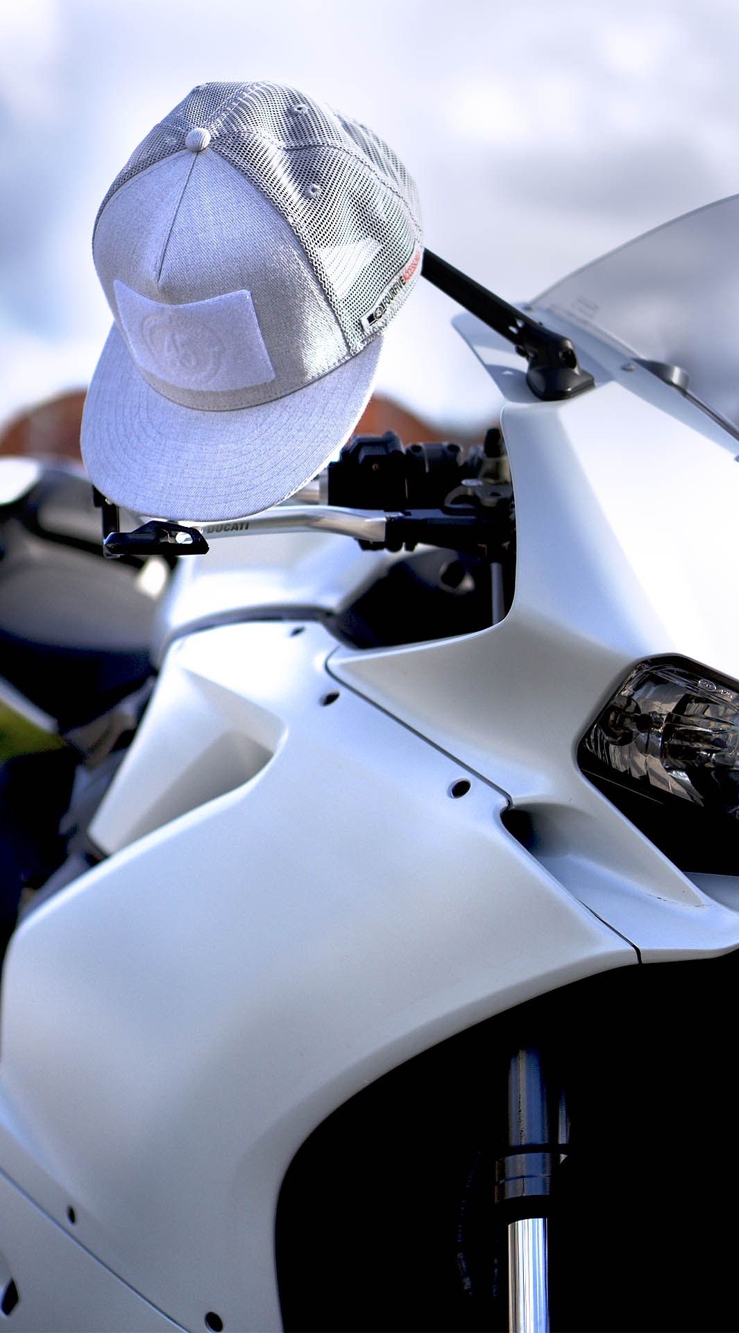 Fourfive white flat brim snap back customizer hat hanging on mirror of white ducati panagale in the summer light.