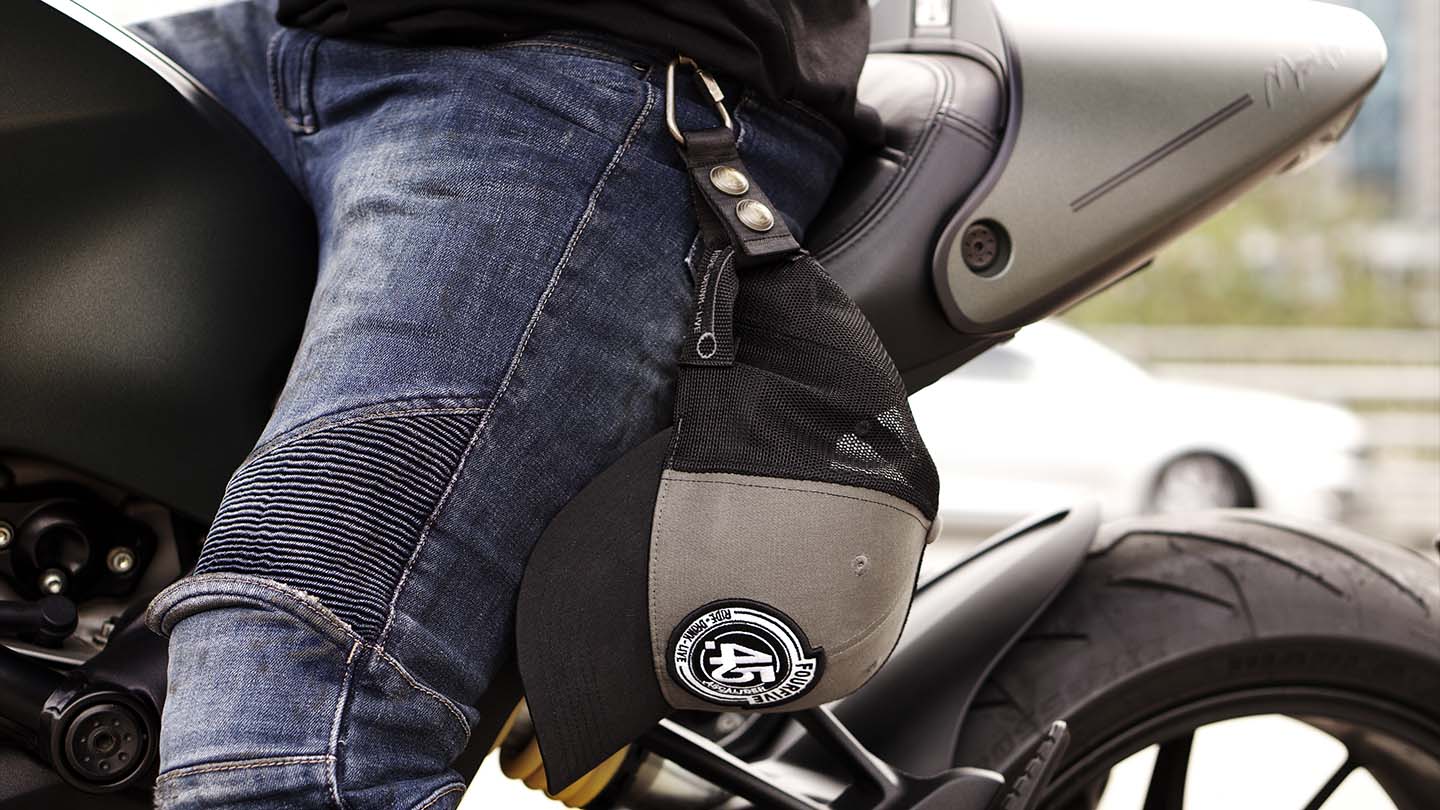 FOURFIVE 45 CURVED BRIM GREY AND BLACK SNAP BACK FLAT TRACKER TRUCKER HAT SECURED TO HAT HOLSTER OF RIDER SITTING ON DUCATI MONSTER 
